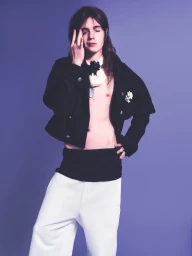Model with long dark hair wearing a black jacket and white trousers against a purple background for HERO Magazine