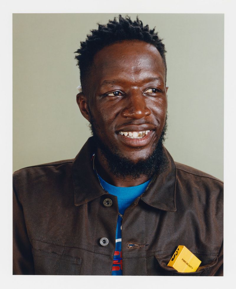 Portrait of an adult Black man with short dark hair and a beard, wearing a dark jacket, smiling and looking to the right side of the frame.