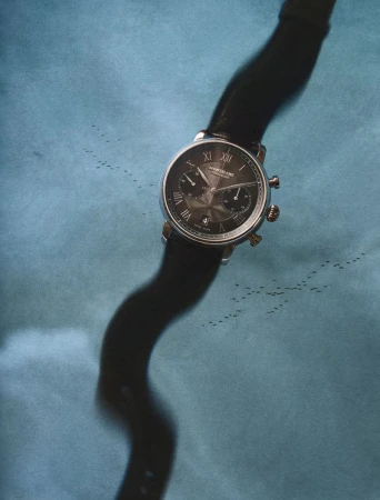 Close-up of a luxury wristwatch with a black leather strap against a mottled blue textured background.