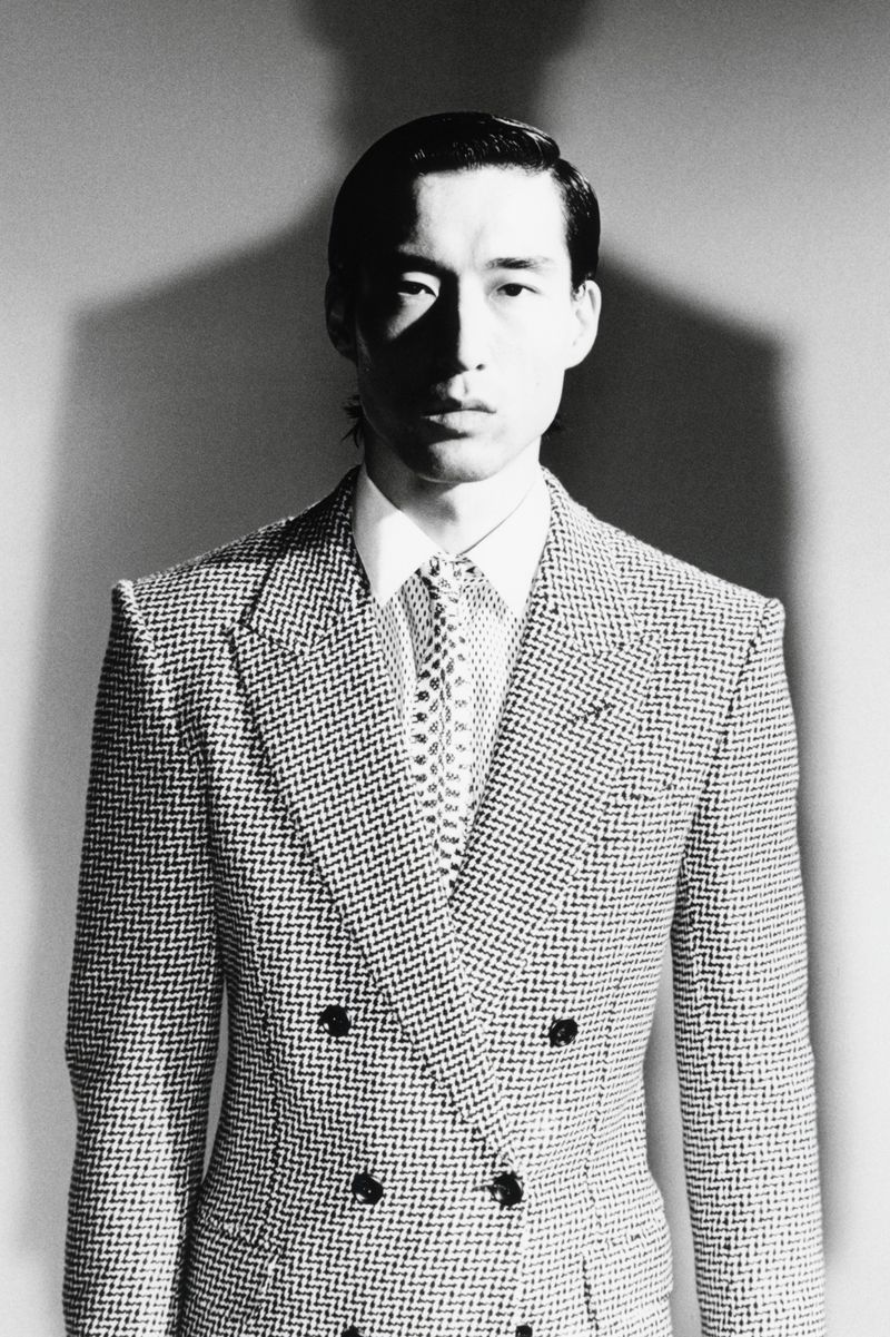 Monochrome portrait of a man wearing a double-breasted patterned suit jacket and patterned tie against a plain backdrop