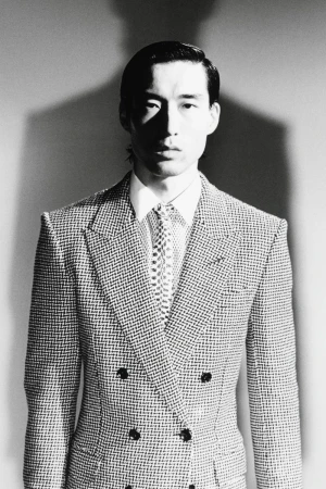 Monochrome portrait of a man wearing a double-breasted patterned suit jacket and patterned tie against a plain backdrop