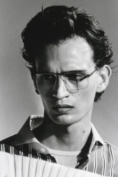 Close-up portrait of a man wearing glasses and a striped shirt against a plain light background.