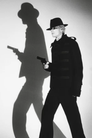 Model in black fedora holding a handgun against a white backdrop with a dramatic large shadow casting a silhouette holding a gun
