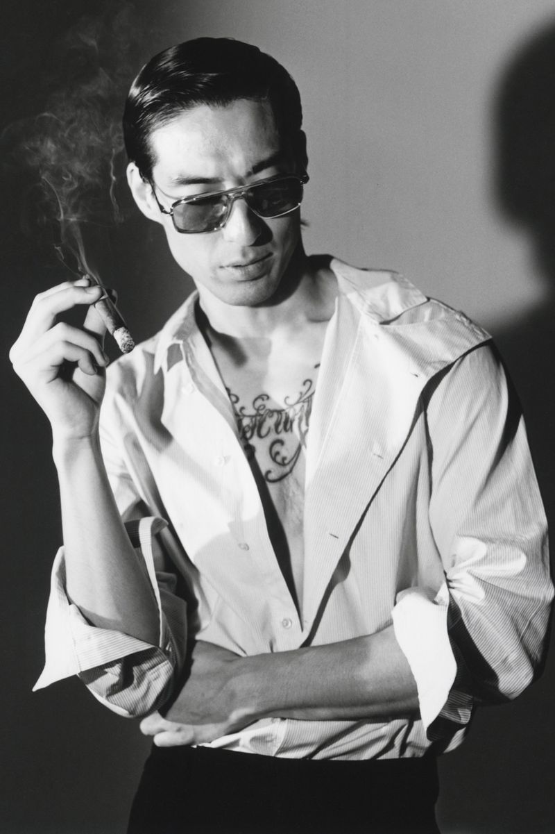 Man wearing sunglasses and a button-down shirt smoking a cigar in a black and white editorial portrait for HERO Magazine