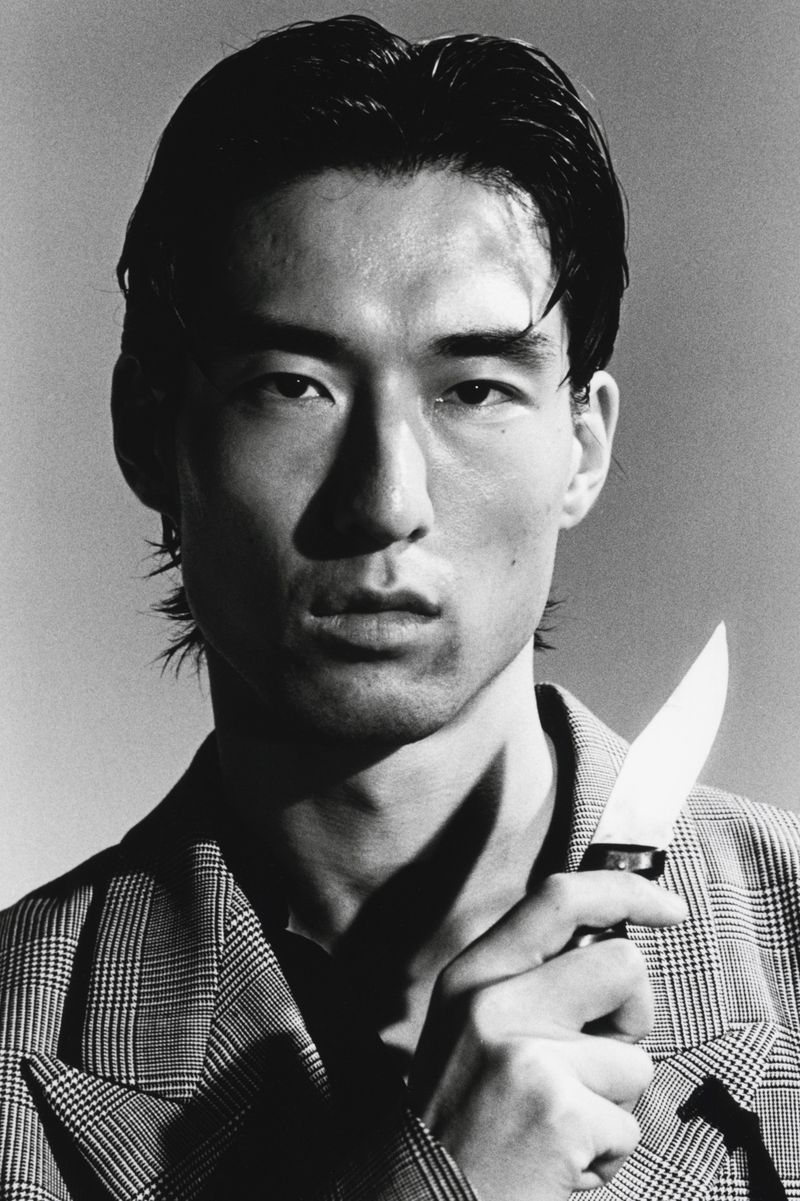 Portrait of an Asian man wearing a plaid blazer holding a knife in a dramatic black and white editorial shoot for HERO Magazine.