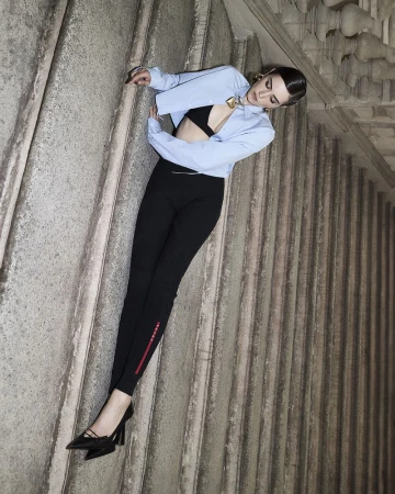 Model Kim Schell posed against ornate stone architectural stairs wearing a light blue cropped shirt and black trousers for Amica Magazine