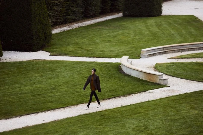 Model walking along a gravel garden path through manicured lawns and sculpted hedges for an Amica Magazine editorial.
