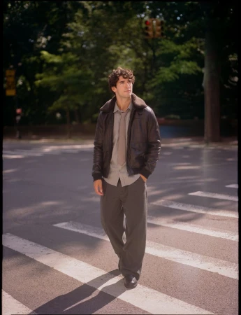 Man wearing a brown leather shearling jacket and trousers crossing a city street