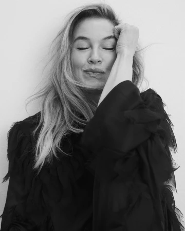 Black and white portrait of Renee Zellweger with eyes closed and hand near forehead wearing a dark textured top