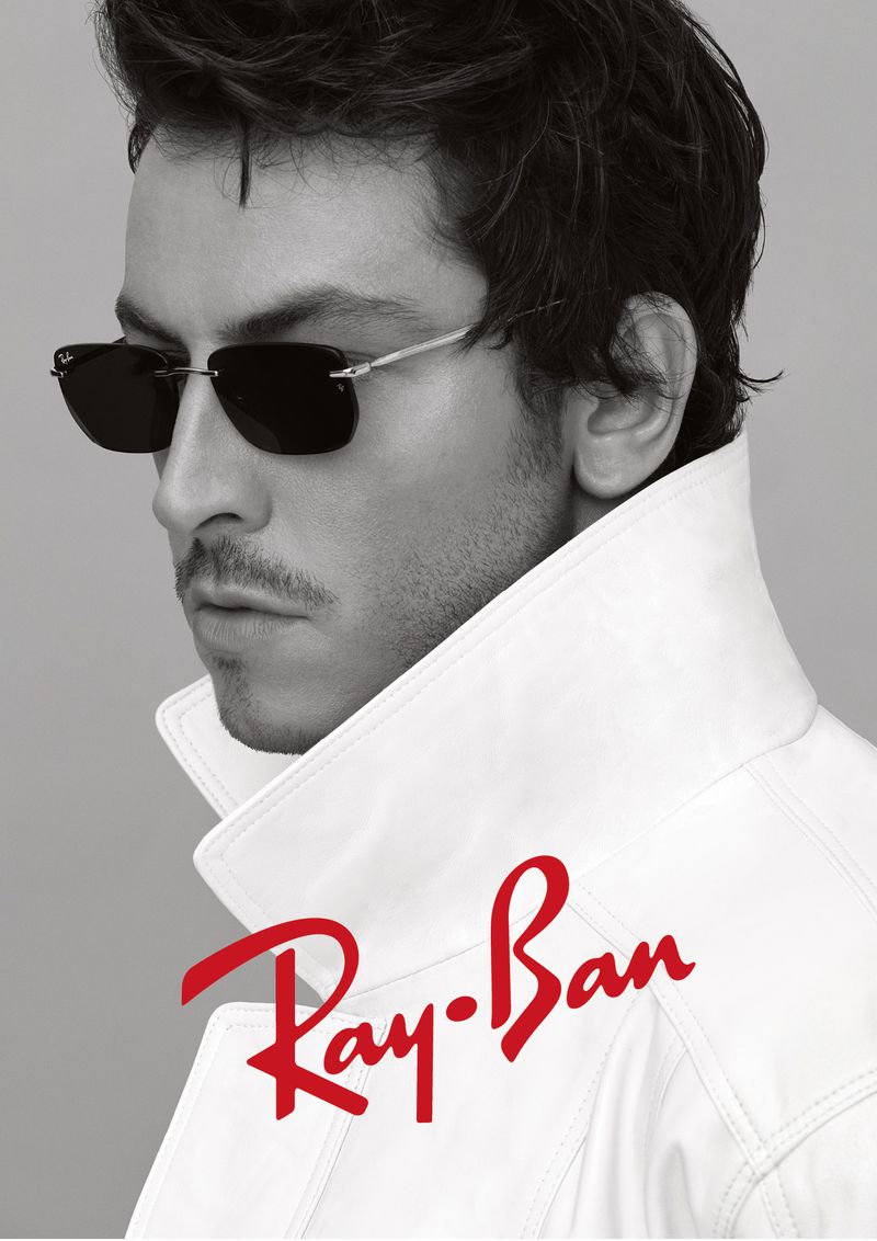 Boran Kuzum wearing dark sunglasses and a white collared jacket against a neutral grey studio background for Ray-Ban.