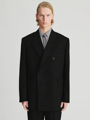 Model in black double-breasted suit jacket with striped shirt and tie against a plain white background