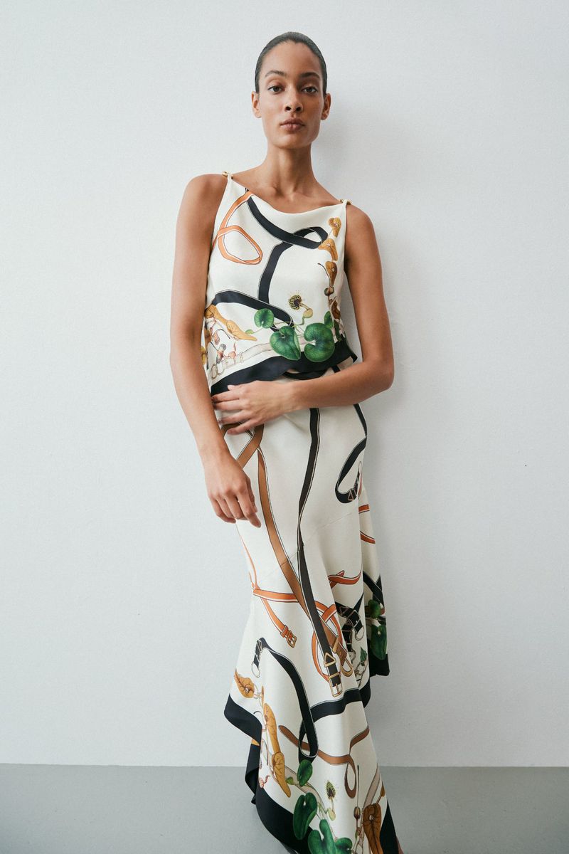 Model in printed silk dress with scarf motifs standing against a neutral studio background