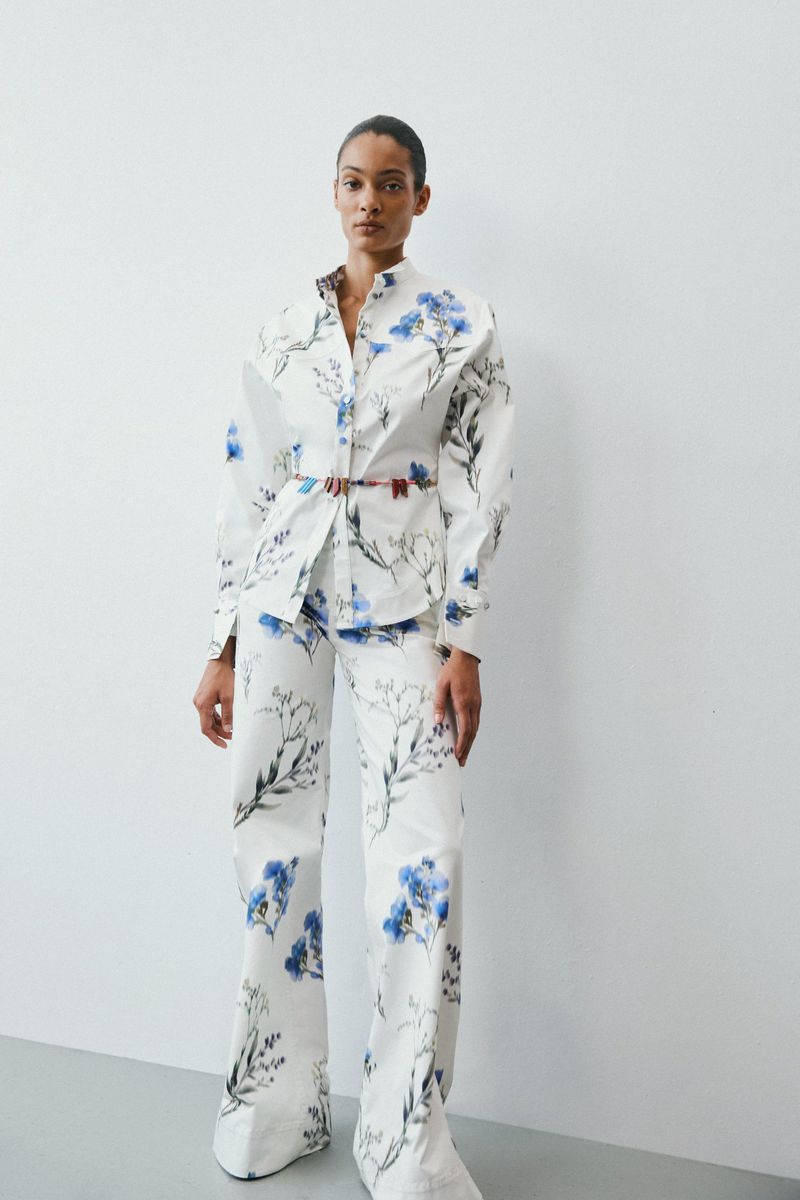 Model standing against a plain white studio background wearing a white matching shirt and trousers with blue floral print.