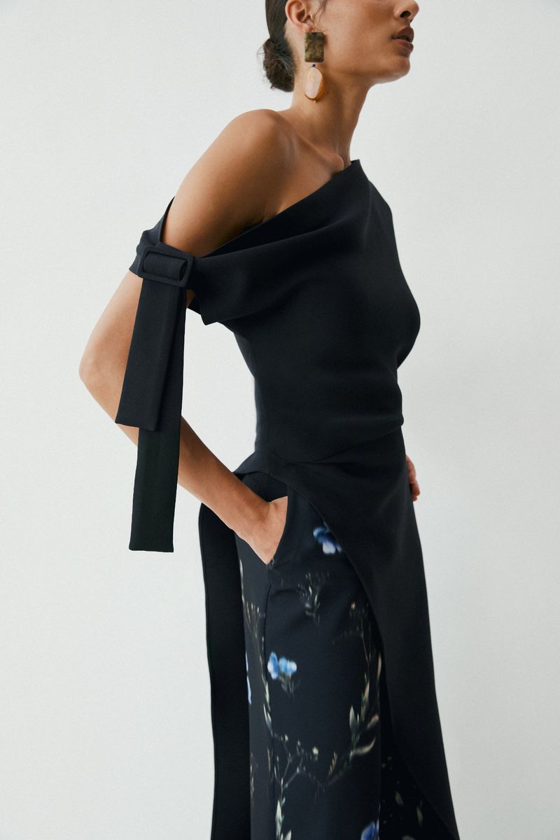 Model wearing a black one-shoulder top and patterned skirt against a plain white background for Amir Taghi Resort lookbook