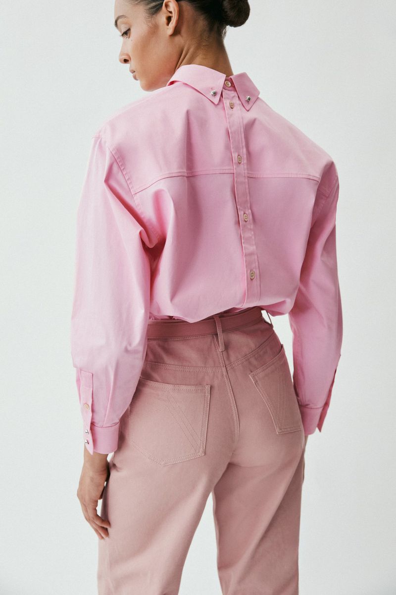 Model seen from behind wearing a pink button-down shirt and pink trousers against a seamless white background