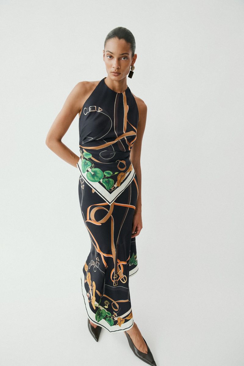 Model in a black patterned halterneck dress posing against a plain white seamless studio background.