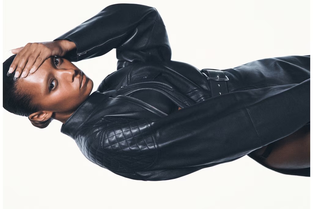 Sophie Wilde in a black leather jacket with her hand to her head against a plain white studio background.