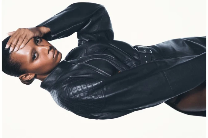 Sophie Wilde in a black leather jacket with her hand to her head against a plain white studio background.