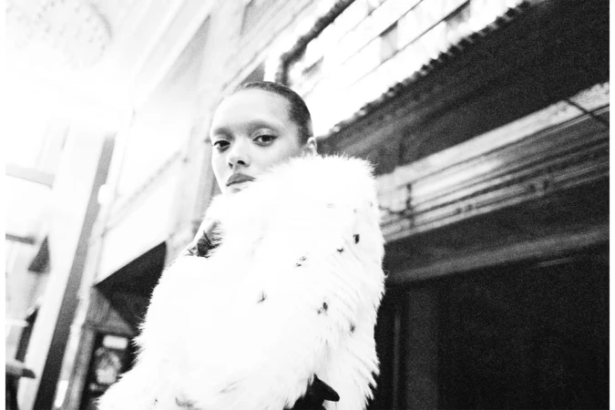 Monochrome portrait of actor Sophie Wilde wearing a textured white fur coat in an interior setting