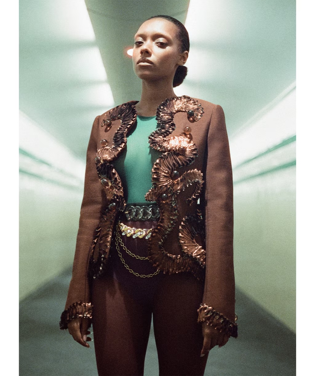 Sophie Wilde wearing an embellished brown jacket and green top in a tunnel-like interior space for Vogue Australia.