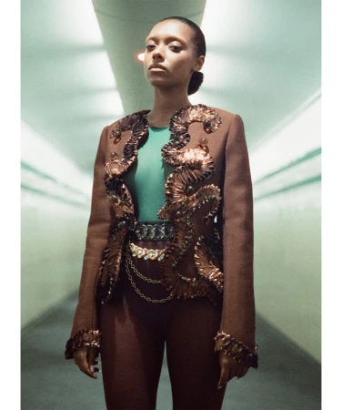 Sophie Wilde wearing an embellished brown jacket and green top in a tunnel-like interior space for Vogue Australia.