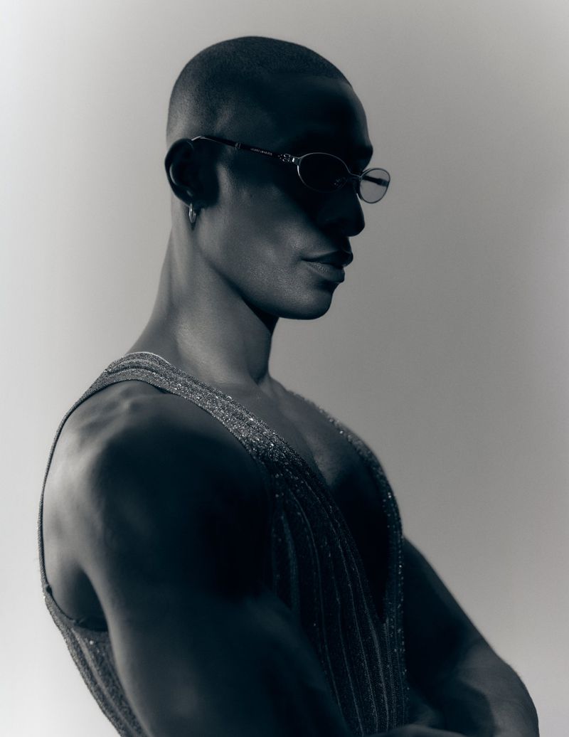 Portrait of a bald Black man wearing sunglasses and a textured sleeveless top against a plain light background.