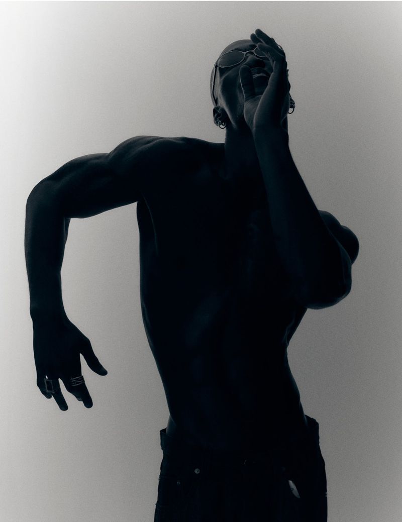 Silhouette of a shirtless man posing dramatically with one hand near his face against a white seamless background