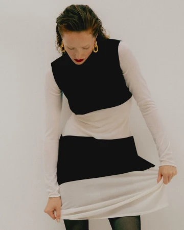 Model wearing a black and white striped dress and gold hoop earrings against a plain white background