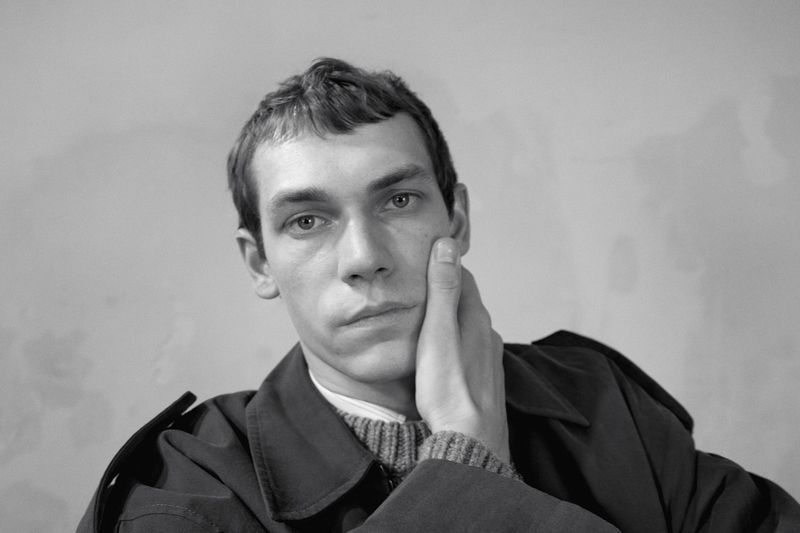 Black and white portrait of a male model with hand on cheek wearing dark coat