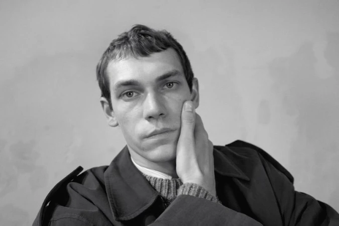 Black and white portrait of a male model with hand on cheek wearing dark coat