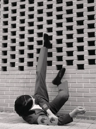 Model lying on the ground with legs kicked up against a textured concrete breeze block wall in GQ Korea editorial.