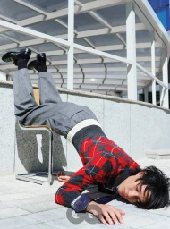 Model in red and grey argyle sweater and grey trousers arched backwards over a modern metal chair outdoors