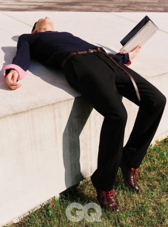 Model lying backward on a concrete ledge holding a laptop, wearing a dark sweater and trousers for GQ Korea LOW BATTERY project