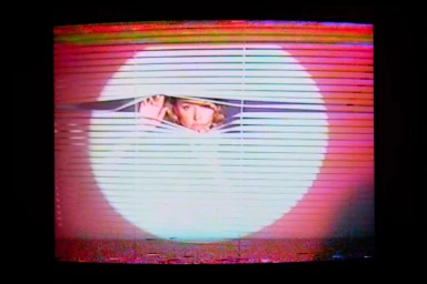 Maika Monroe looking through window blinds with heavy VHS static and scan lines on a CRT television screen