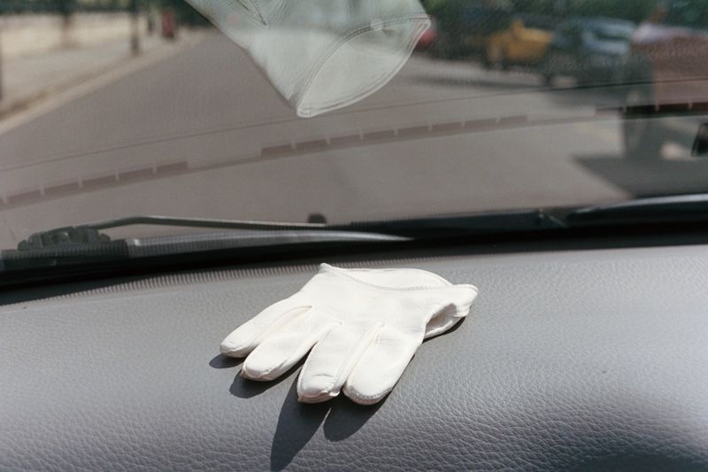 A white leather glove rests on the dashboard of a car with a street visible through the windshield.