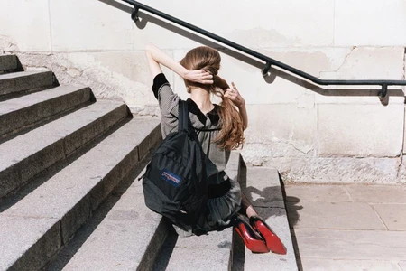 Woman with long hair wearing a patterned dress and black backpack sitting on stone outdoor stairs