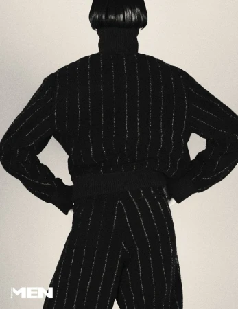 Model seen from behind wearing a black pinstripe turtleneck sweater and matching trousers against a pale background