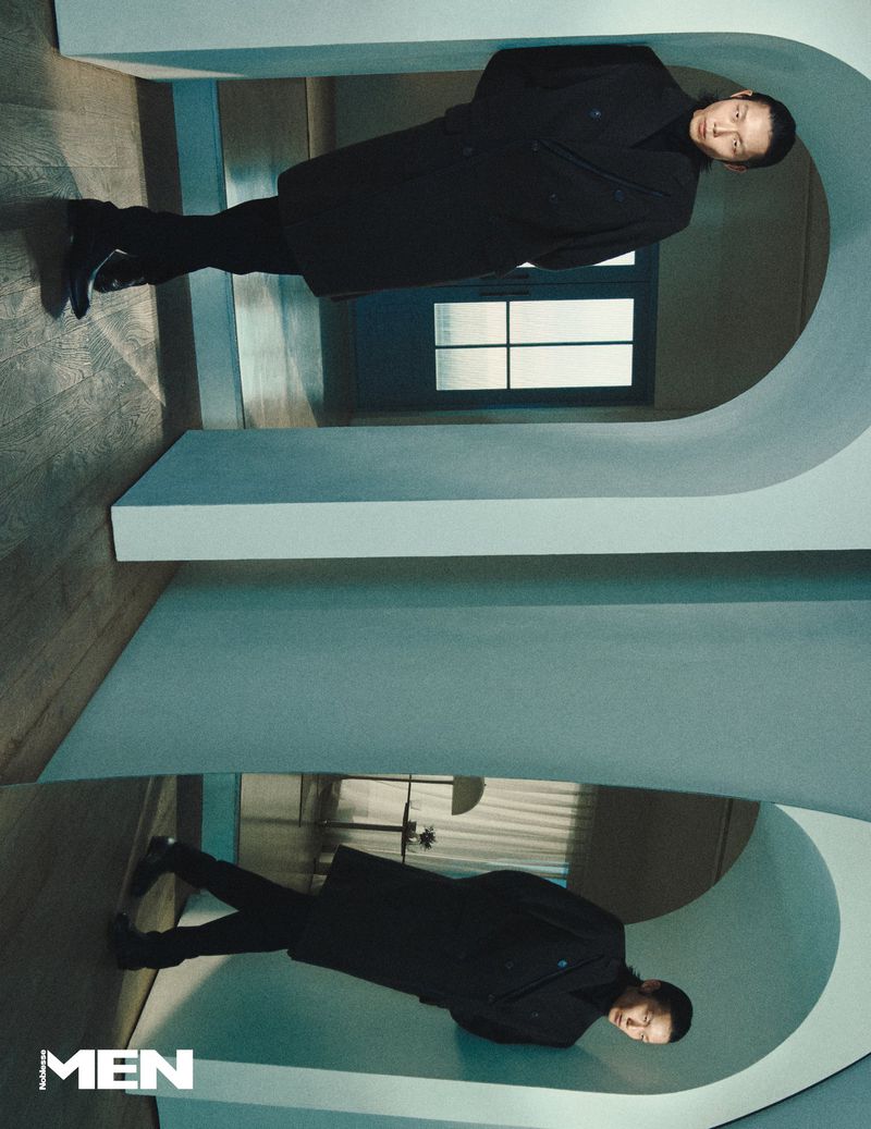 Model Xu Meen wearing a dark coat standing inside an architectural hallway with arched structural dividers.
