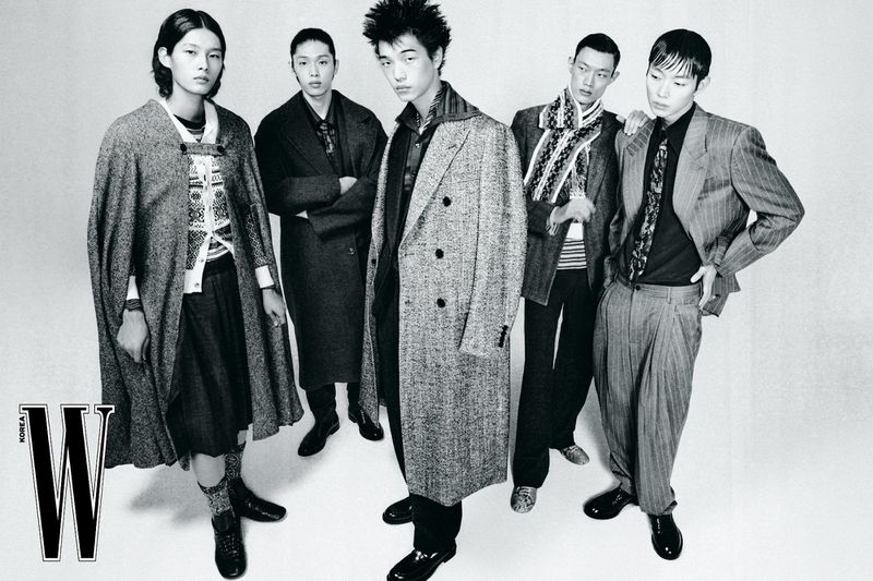 Monochrome fashion editorial image of five Asian male models in tailored coats and patterned knitwear posing against a white studio background.