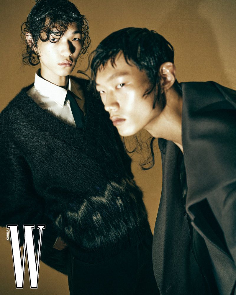 Two male models with styled wet hair wearing dark tailored garments in a fashion editorial for W Korea.
