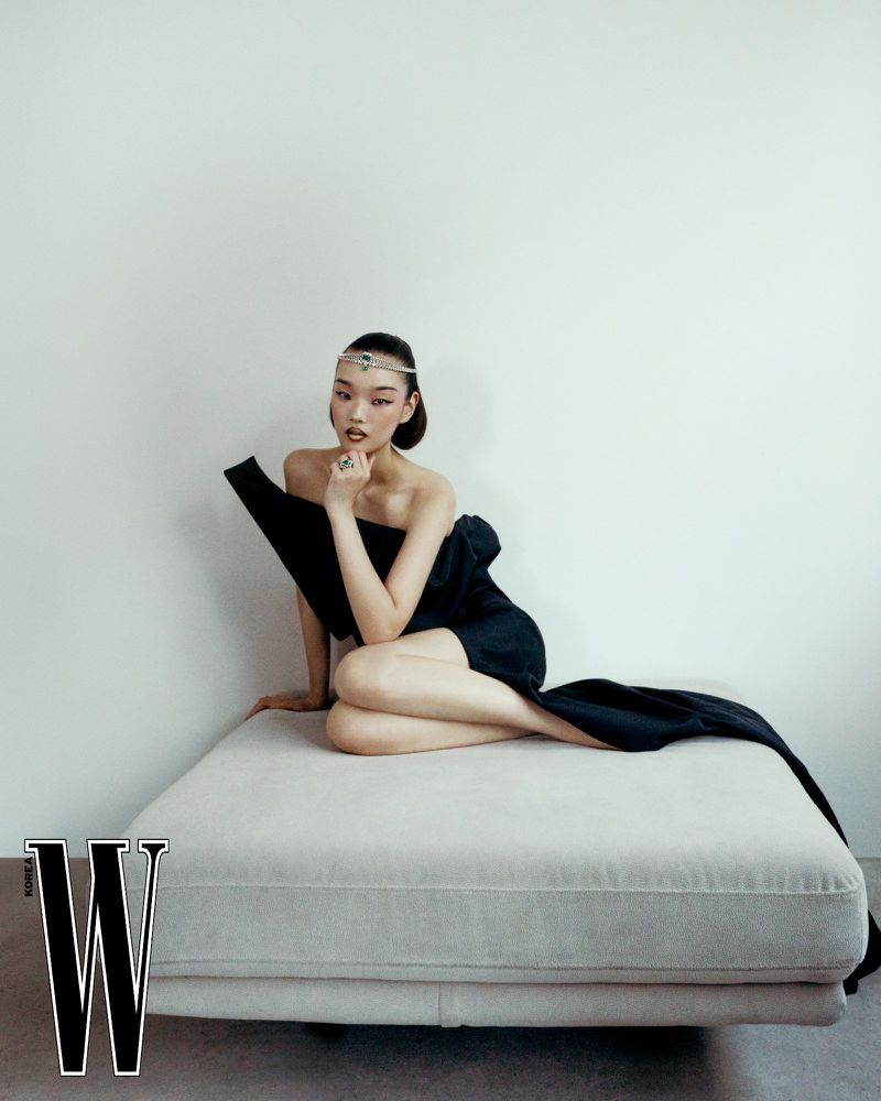 Model wearing a black dress and diamond headpiece seated on a low cushion against a white studio background for W Korea.