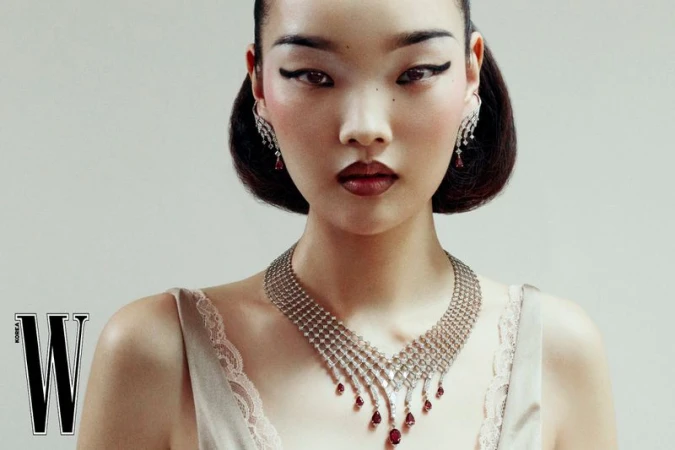 Close-up portrait of an Asian model wearing an elaborate diamond necklace and drop earrings against a neutral background.