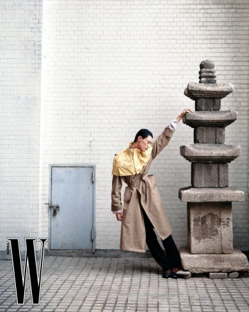 Model Hoyong Kim leaning against a stone pagoda, wearing a brown trench coat with a yellow cape detail.