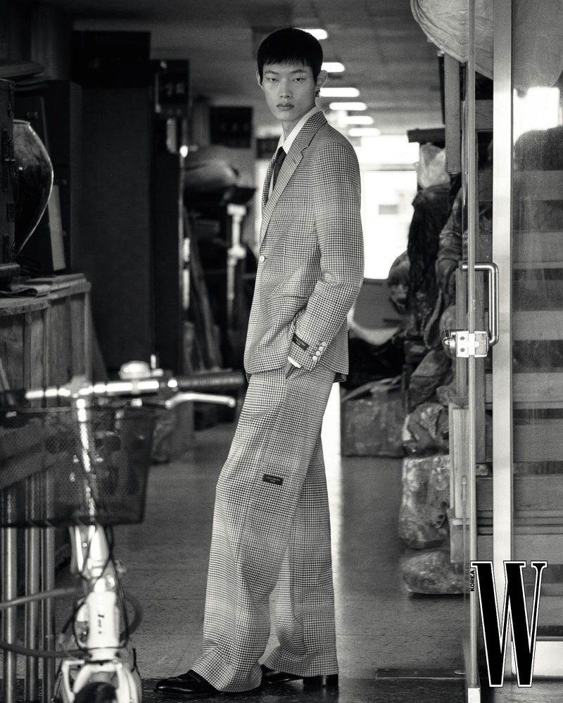 Model Hoyong Kim in a patterned suit standing inside a shop corridor, shot by photographer Park Jongha for W Korea.