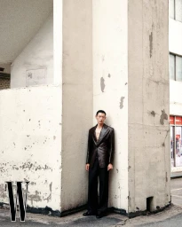 Model Hoyong Kim standing against a weathered concrete pillar wearing a dark blazer and trousers for W Korea