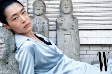 Model in a pale blue blouse reclining near carved stone statues and a tiled wall for W Korea editorial.