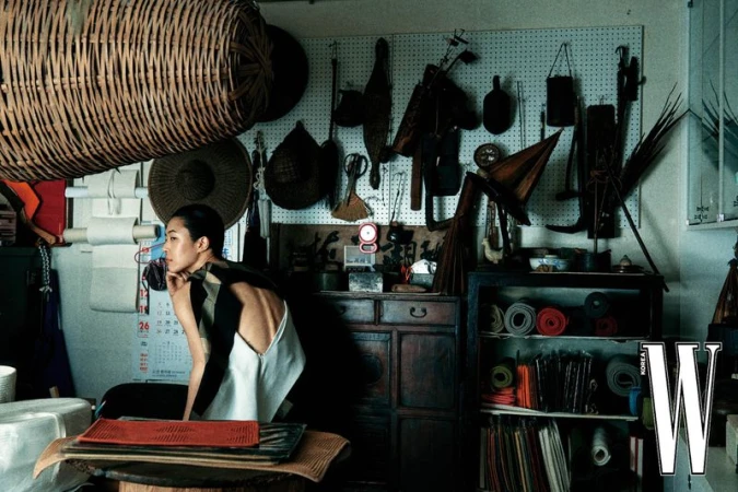 Model seated in an antique market surrounded by woven baskets and traditional crafts for W Korea