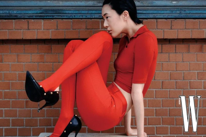 Model in a red polo top, red tights, and black high heels posed against a red brick wall for W Korea.