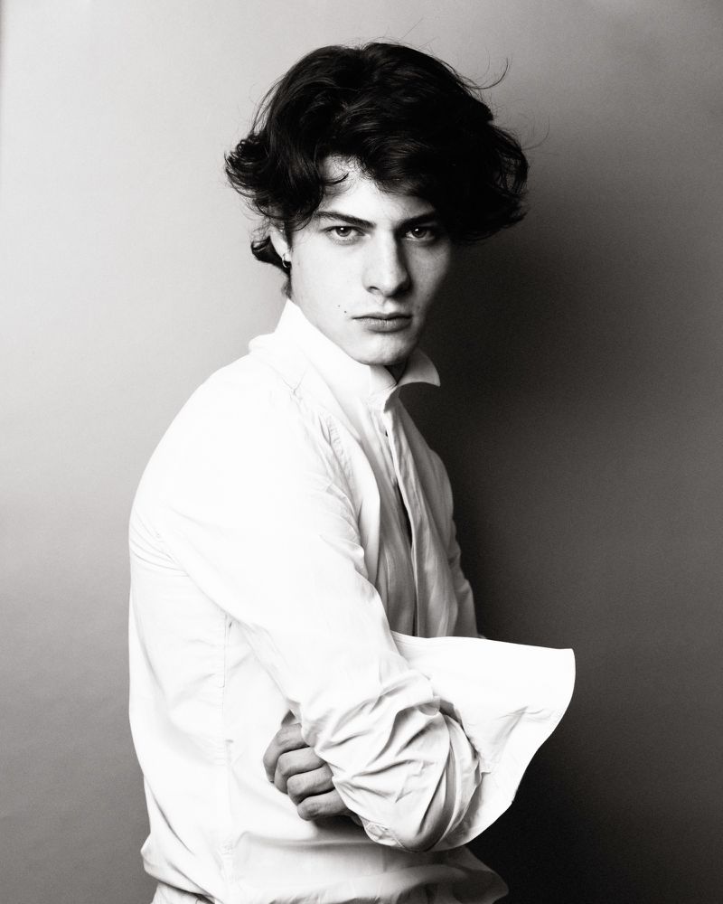 Portrait of young man with dark wavy hair in white button-down shirt against plain studio background