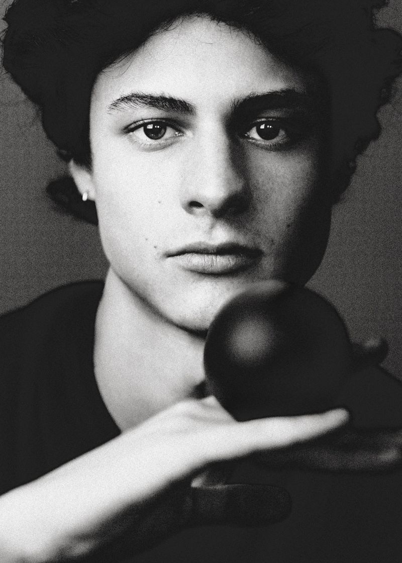Close-up portrait of a young man holding a dark sphere in front of his face in monochrome